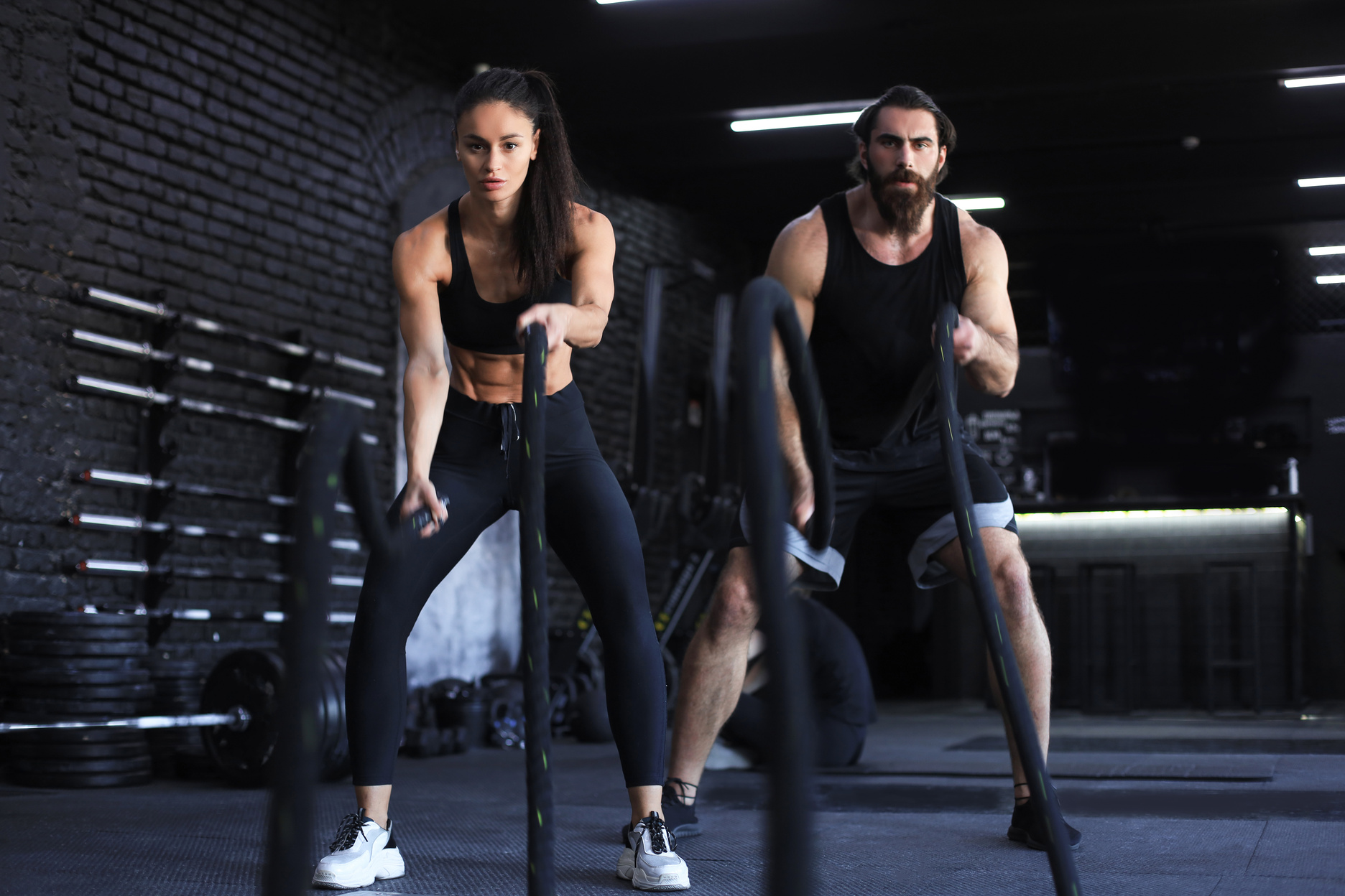 Athletic young couple with battle rope doing exercise in functional training fitness gym.